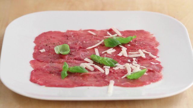 Beef carpaccio being sprinkled with grated parmesan