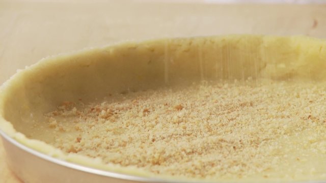A shortbread base being sprinkled with breadcrumbs