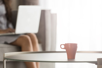 A cup of coffee with Young woman using laptop at home, selective focus on cup of coffee, vintage...