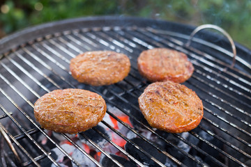 Juicy beef burgers sizzling on a charcoal BBQ with glowing red charcoal