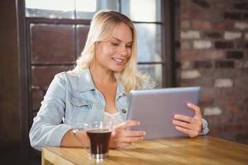 Smiling blonde having coffee and using tablet computer