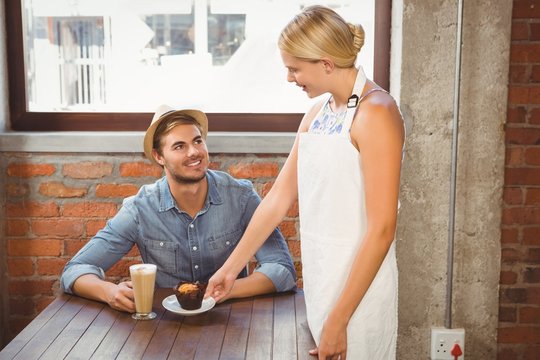Smiling blonde waitress serving muffin to handsome hipster