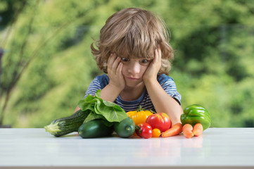 Fototapeta na wymiar Cute little boy sitting at the table, unhappy with his vegetable meal, bad eating habits, nutrition and healthy eating concept