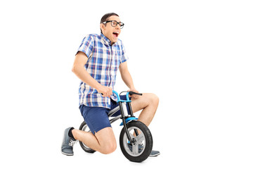 Fototapeta na wymiar Silly young guy riding a tiny bicycle