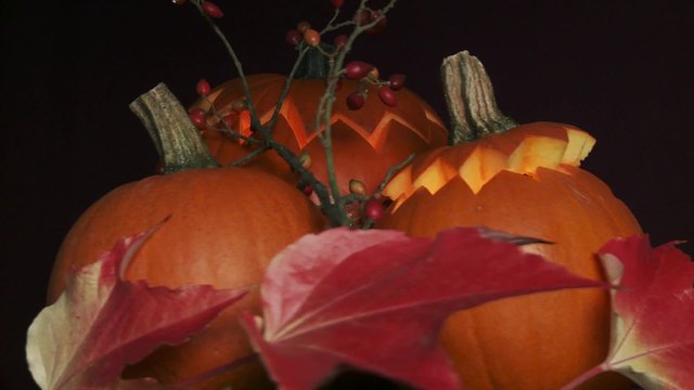 Illuminated Halloween pumpkins with autumn leaves and rose hips