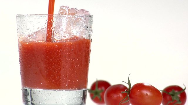Pouring tomato juice into a glass filled with ice cubes