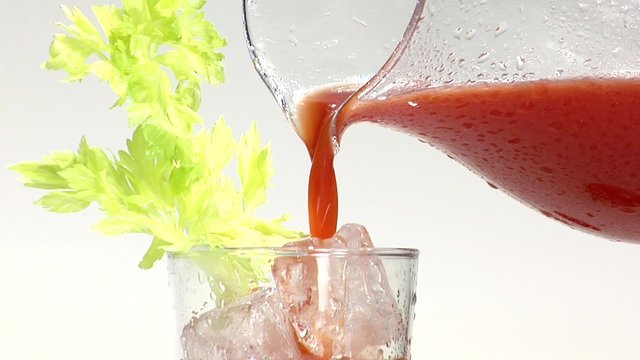 Pouring tomato juice into a glass with celery and ice