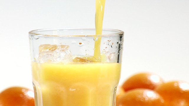 Pouring orange juice into a glass of ice cubes