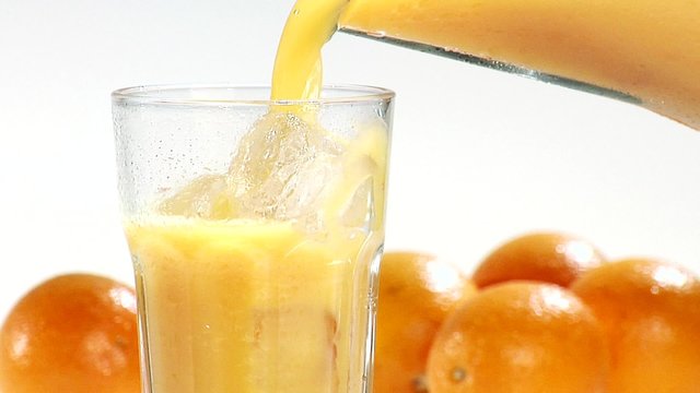 Pouring orange juice into a glass of ice cubes