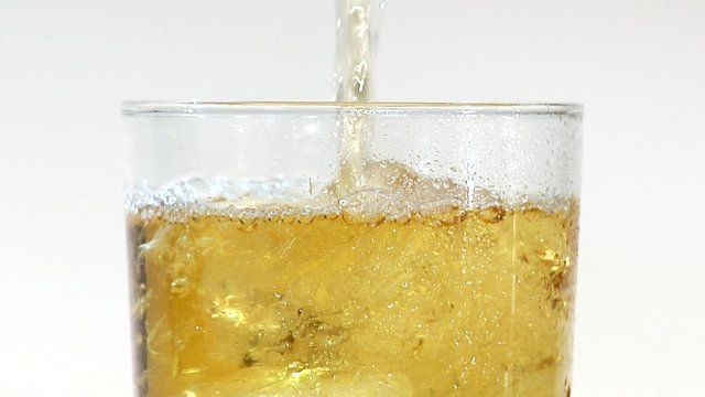 Pouring apple juice into a glass of ice cubes (close-up)