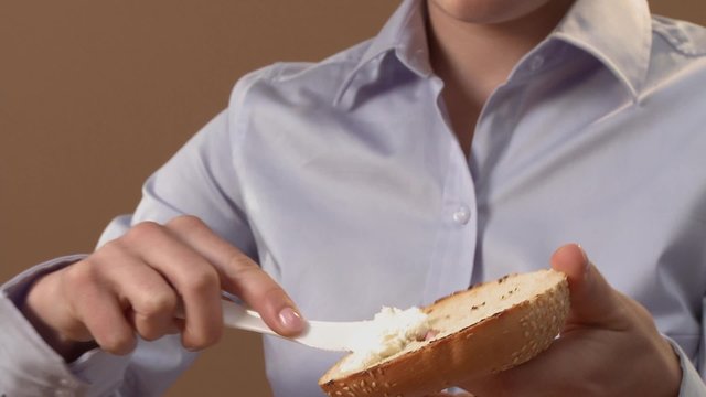 Young woman spreading cream cheese on half a bagel