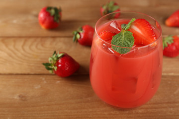 Glass of fresh strawberry juice on wooden background