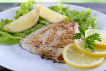 Dish of fish fillet with lettuce and lemon on plate close up