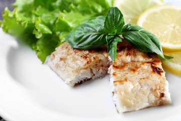 Dish of fish fillet with greens and lemon on plate close up