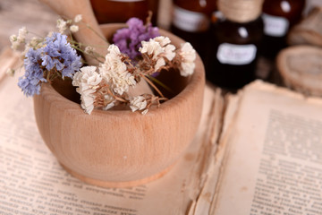 Old book with dry flowers in mortar and bottles on table close up