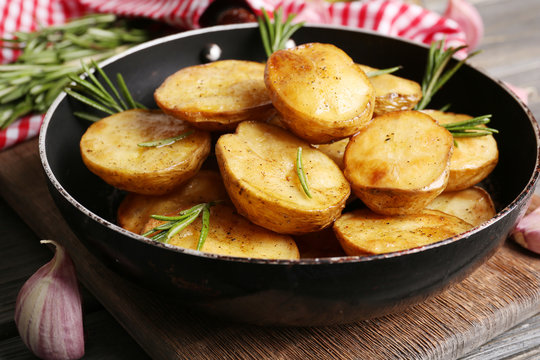 Delicious baked potato with rosemary in frying pan on table close up