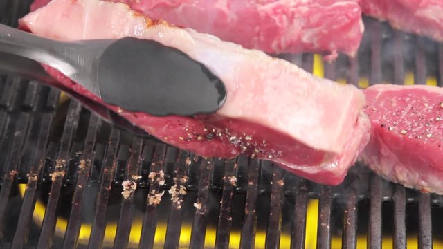 New York strip steaks being turned on a grill