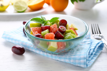 Fruit salad in glass bowl, on light wooden background