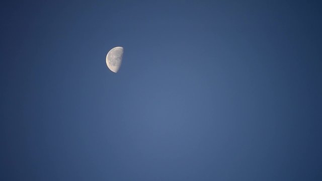 Moon moving across cloudless blue sky