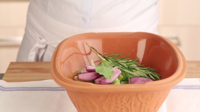 Herbs being added to vegetables in a terracotta baking dish