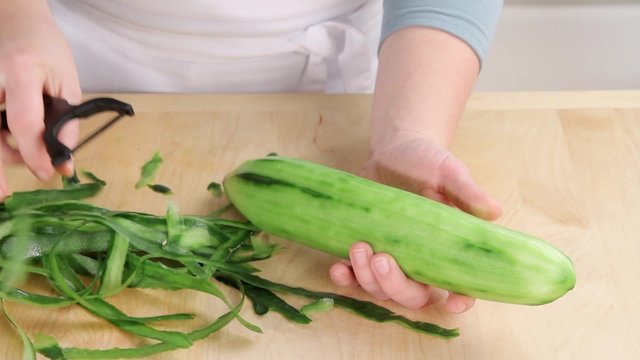A cucumber being peeled and cut in half lengthways