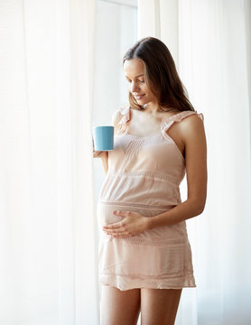 happy pregnant woman with cup drinking tea at home