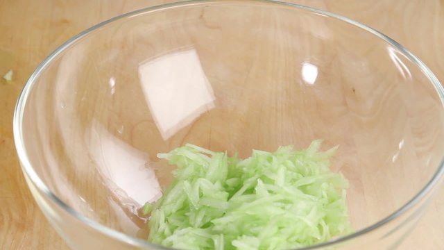 Grated cucumber in bowl being seasoned with salt