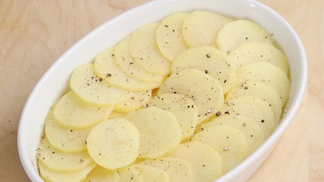 Potato slices in a baking dish being seasoned with nutmeg