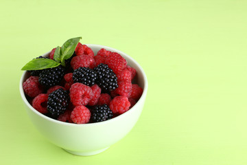raspberries and blackberries in a bowl of light green background