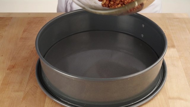 A biscuit crumb and butter mixture being spread into a springform tin