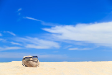 Sunglasses over coconut fruit on sandy beach under hot shiny sun