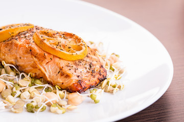 Portion of grilled salmon with lemon and sprouts.