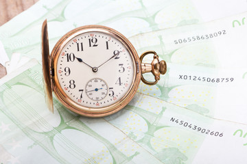 Time is money concept with hundred euro bills and golden pocket watch.