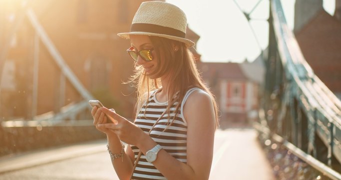 Woman using smartphone in the European city. Slow Motion, 4K. Hipster girl browsing Internet on a phone, texting and communicating outdoors. Travel. Lens flare. 