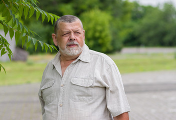 Outdoor portrait of a bearded senior man in light shirt looking into the distance with hope