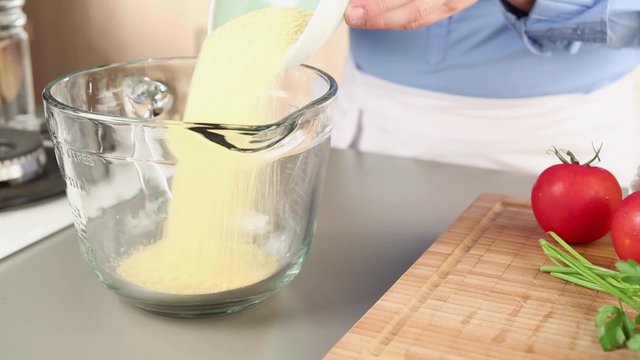 Lukewarm water being poured over bulgur in a glass bowl