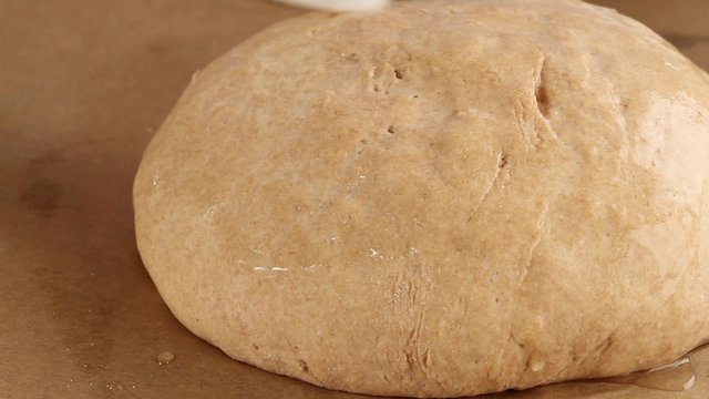 A loaf of bread being brushed with water, scored and sprinkled with sunflower seeds (close-up)