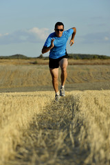 sport man with sunglasses running outdoors on straw field ground in frontal perspective