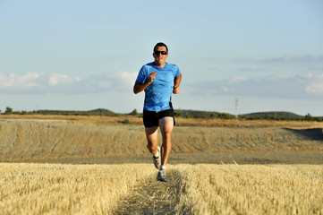 sport man with sunglasses running outdoors on straw field ground in frontal perspective