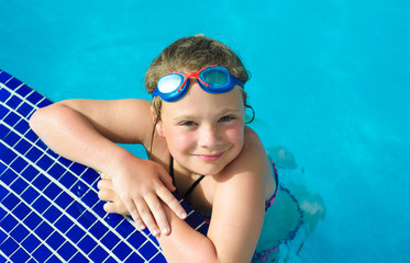 Naklejka premium Smiling little girl in swimming goggles in the swimming pool