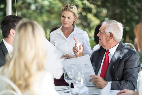 Waitress explaining menu to clients at table