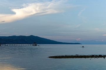 A Blue Morning. There are a few people around, boats are left on the shore, and the water has receded outwards.
