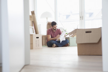 Young man in new flat with cardboard boxes holding ground plan