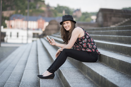 Germany, Koblenz, Deutsches Eck, young woman with cell phone sitting on stairs