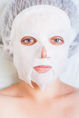 Woman relaxing in spa salon applying white face mask