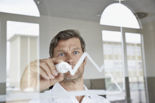 Businessman drawing diagram on glass pane in office