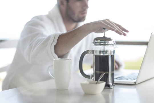 Close-up of man with coffee plunger using laptop