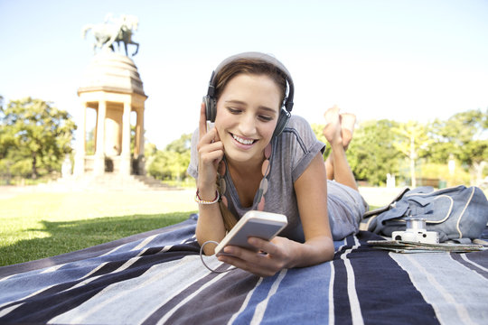 Young woman lying on blanket in park listening to music