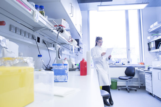 Young female scientist working at biological laboratory reading protocol