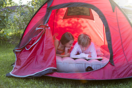 Boy and girl reading lying in a red tent with a book